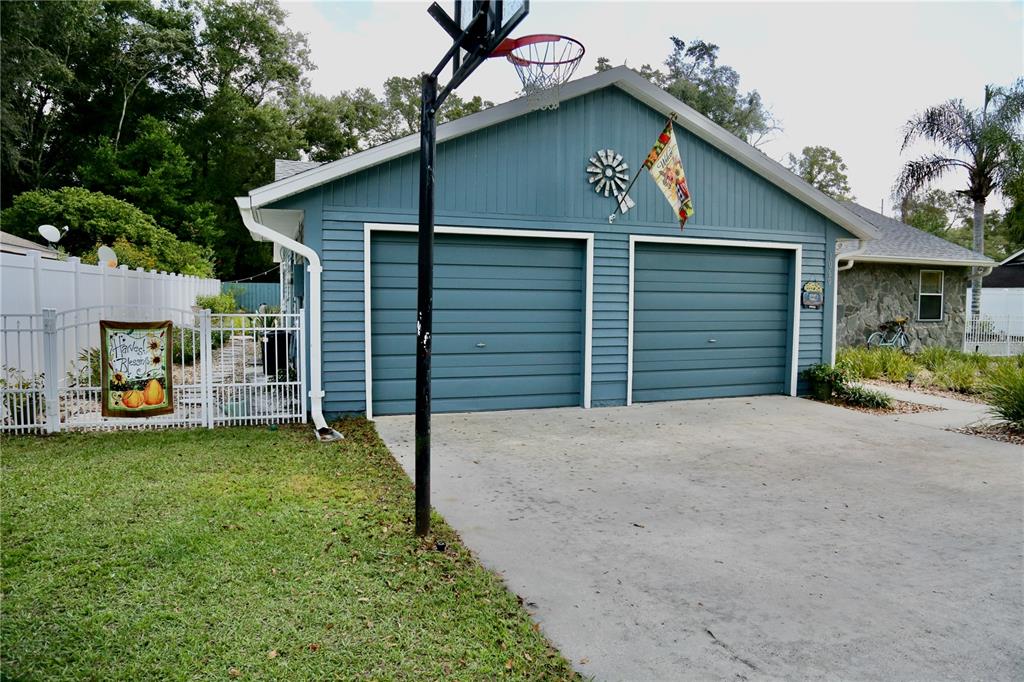 A blue detached two-car garage with a basketball hoop stands next to a white fence — 1069 SE 57TH AVENUE, OCALA, FL