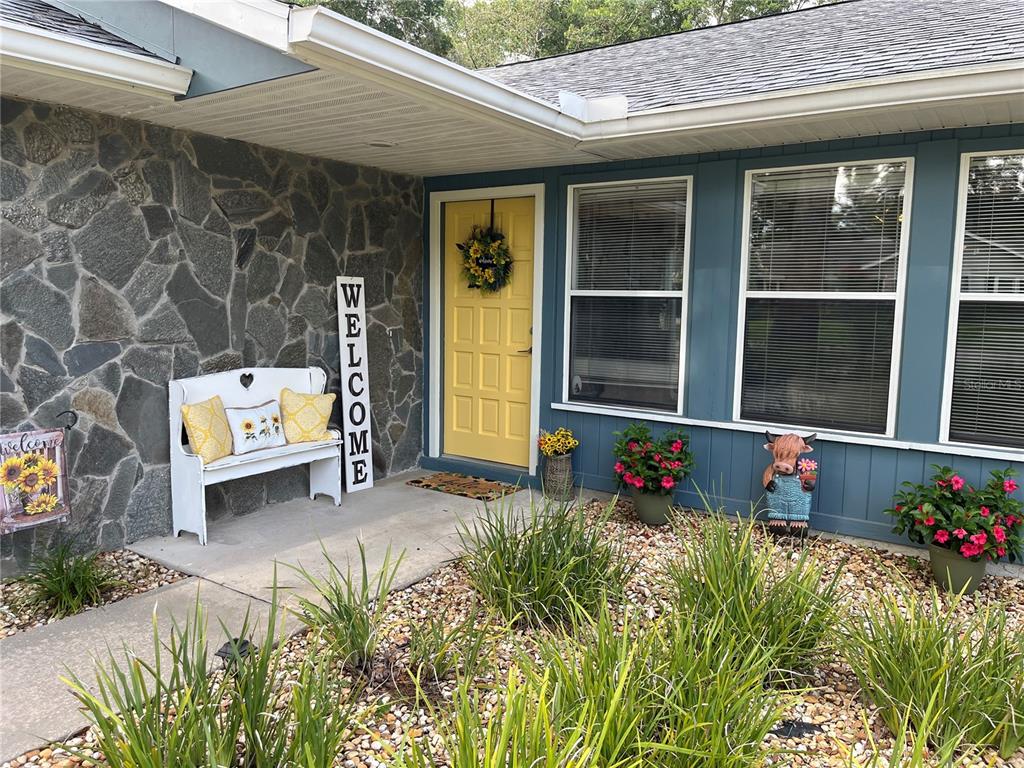 A yellow front door is centered on a house exterior with stone siding and landscaping — 1069 SE 57TH AVENUE, OCALA, FL
