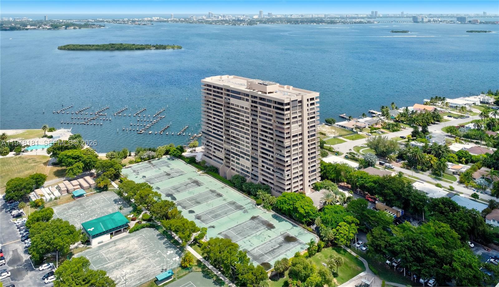 An aerial view shows a tall residential building next to tennis courts and a bay — 11113 Biscayne Blvd, Miami FL 33181, MIAMI, FL