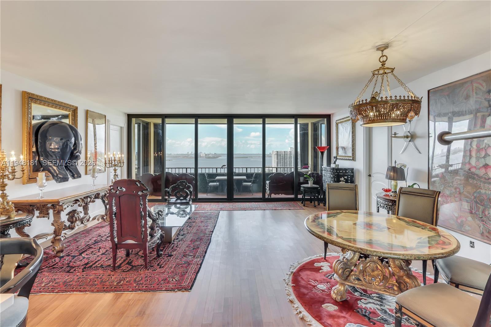 A spacious living and dining area features hardwood floors, ornate furniture, and floor-to-ceiling balcony windows — 11113 Biscayne Blvd, Miami FL 33181, MIAMI, FL