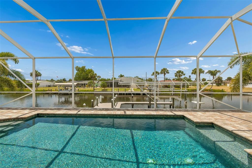 A swimming pool sits inside a screened lanai overlooking a canal with a boat dock — 4462 EWING CIRCLE, PORT CHARLOTTE, FL