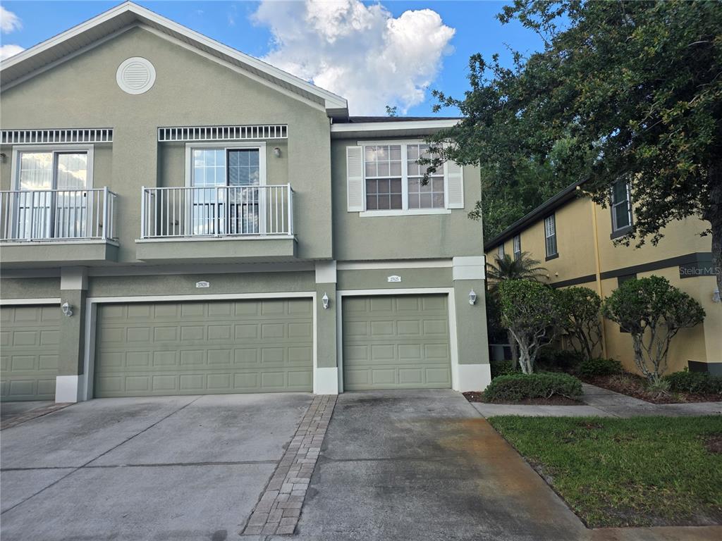 A two-story townhouse exterior features two garage doors, a balcony, and light green stucco siding — 27625 PLEASURE RIDE LOOP, WESLEY CHAPEL, FL