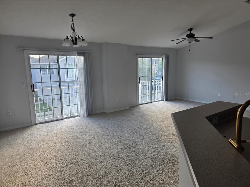 A living area features beige carpet, two sliding glass doors, a ceiling fan, and chandelier — 27625 PLEASURE RIDE LOOP, WESLEY CHAPEL, FL