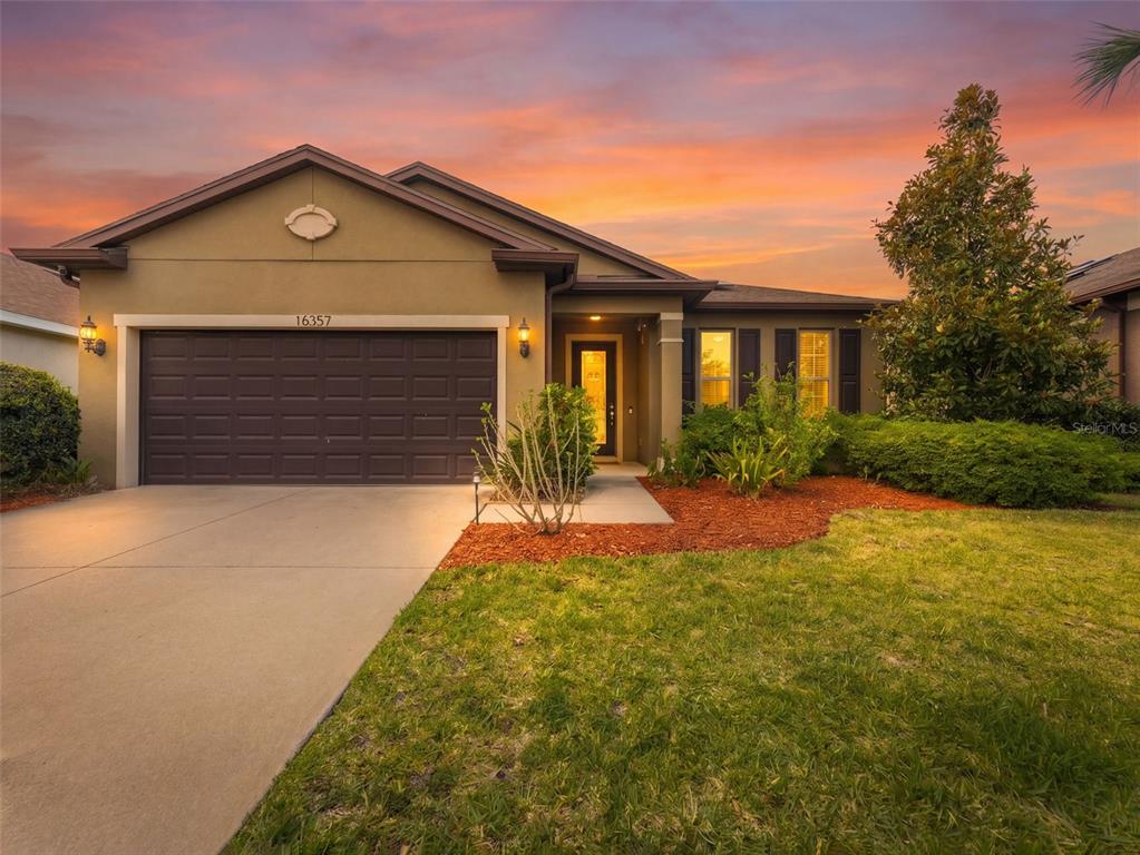 A single-story house with a brown garage, beige stucco exterior, and a landscaped front yard — 16357 TREASURE POINT DRIVE, WIMAUMA, FL