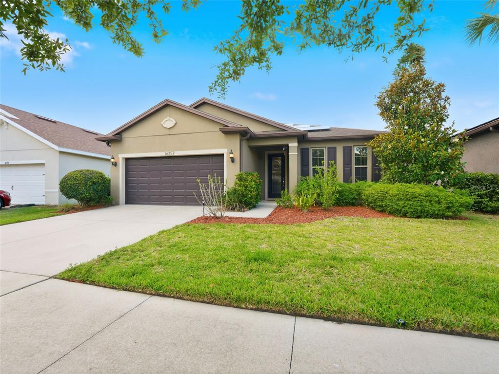 A single-story house with a brown garage, tan stucco exterior, and a manicured front lawn — 16357 TREASURE POINT DRIVE, WIMAUMA, FL