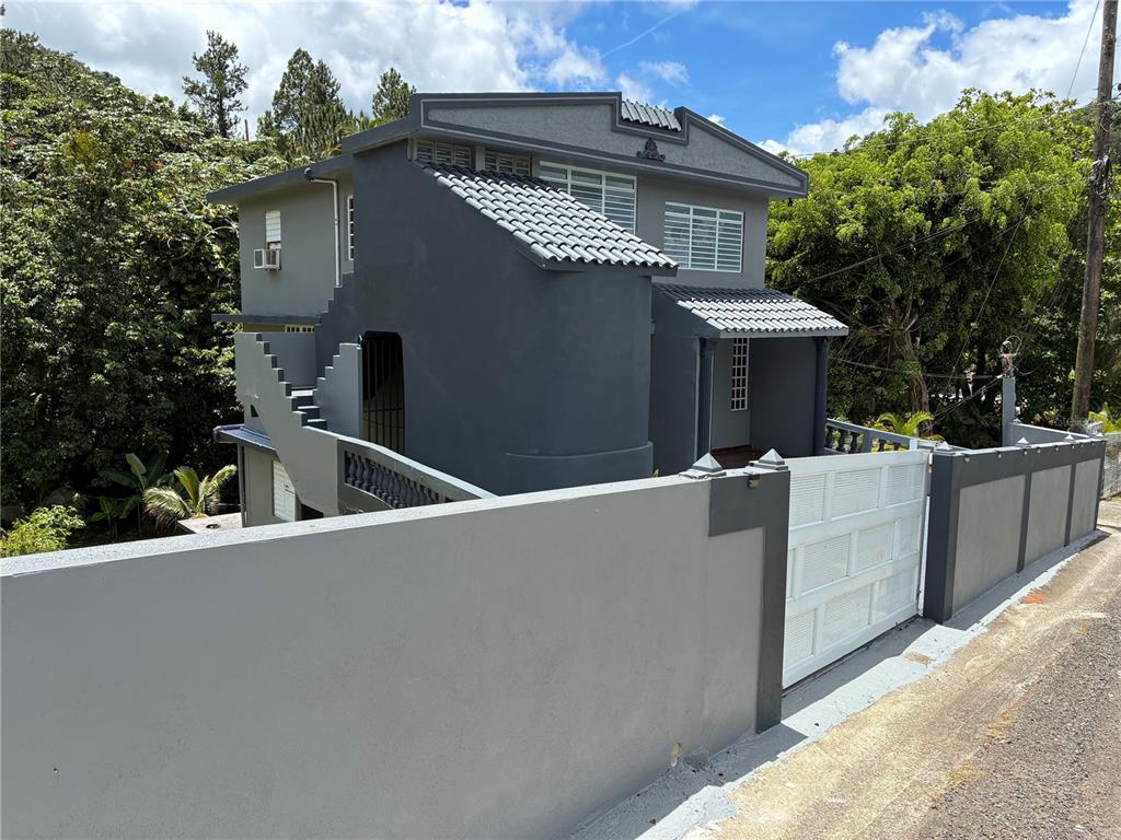 A two-story gray house with a tiled roof stands behind a concrete perimeter wall — 743 KM 4.3 LA VEGA, GUAVATE UNIT 1, CAYEY, PR