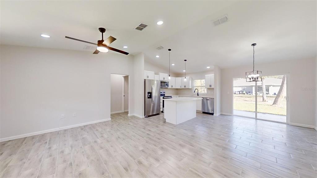 An open-concept kitchen and living area features light wood-look tile floors and white cabinetry — 217 OAK LANE ROAD, OCALA, FL