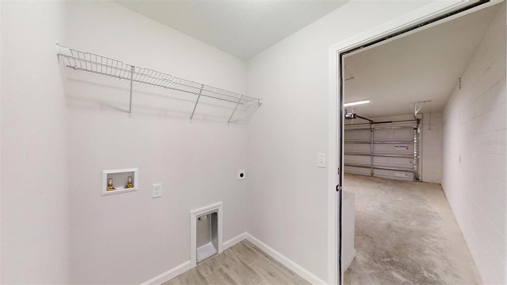 A laundry room with a wire shelf and utility hookups, leading into a concrete garage — 217 OAK LANE ROAD, OCALA, FL