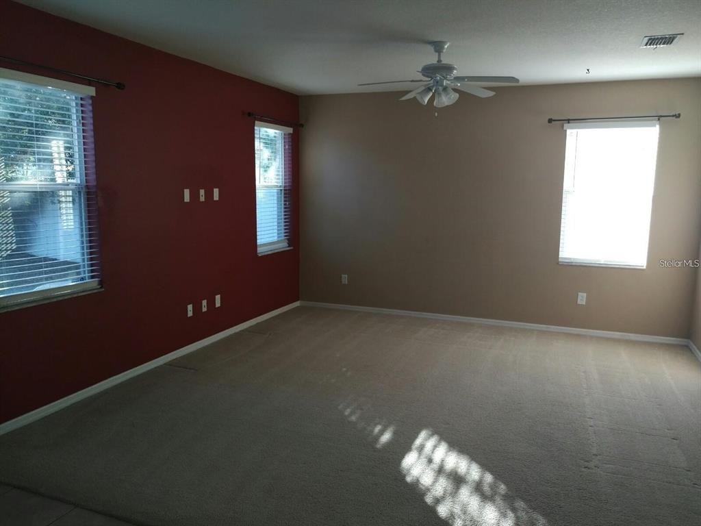 An empty living room features beige carpet, tan walls, a red accent wall, and ceiling fan — 5804 JUSTICIA LOOP, LAND O LAKES, FL