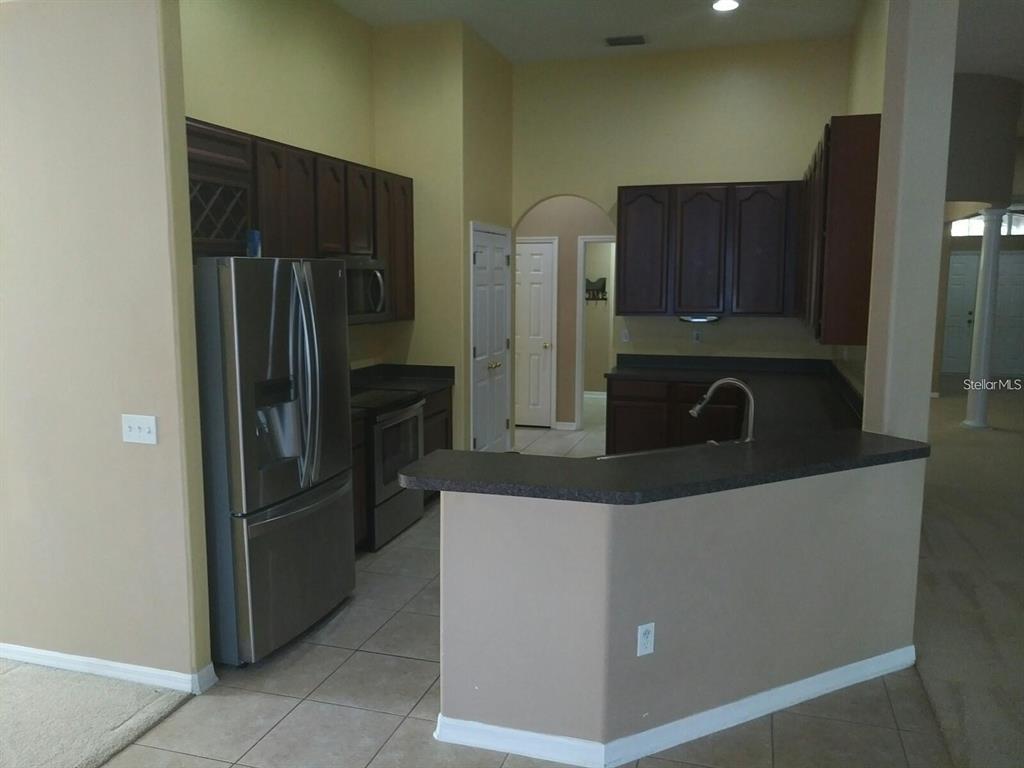 A kitchen features dark wood cabinets, stainless steel appliances, and a peninsula with dark countertops — 5804 JUSTICIA LOOP, LAND O LAKES, FL
