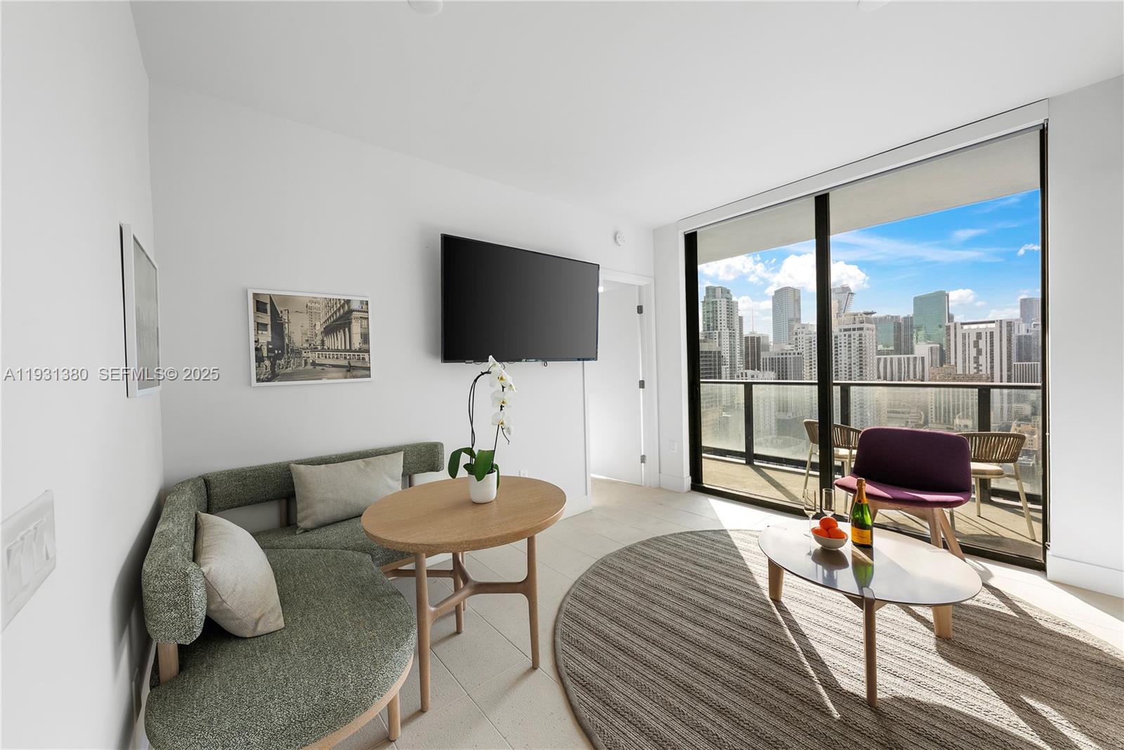 A modern living room features a curved green sofa, a television, and a balcony view — 159 NE 6th St # 2608, Miami FL 33132, MIAMI, FL