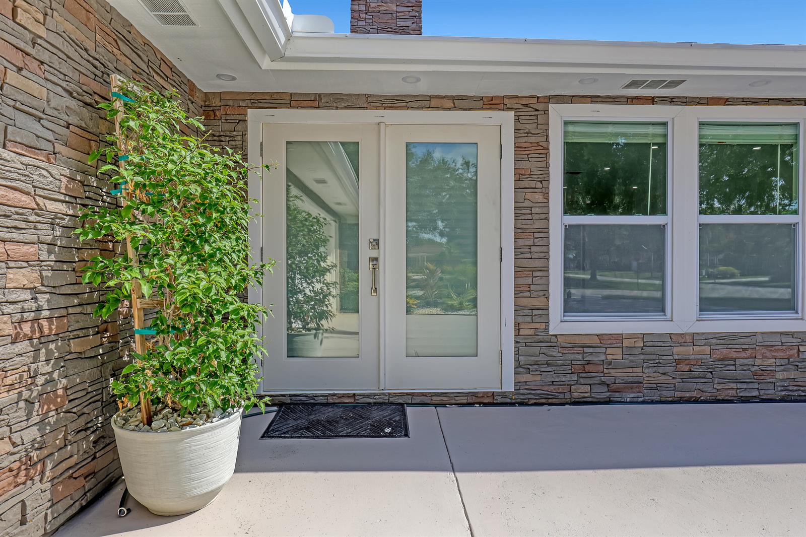 A stone-clad exterior wall features double glass doors and a potted plant on a patio — 6185 White Oak Court, Jupiter FL 33458, JUPITER, FL