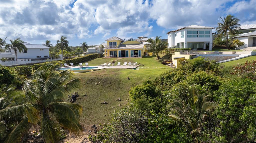 A yellow house with a pool sits on a grassy hill near other coastal homes — 5 BEACH VILLAGE, VIEQUES, PR