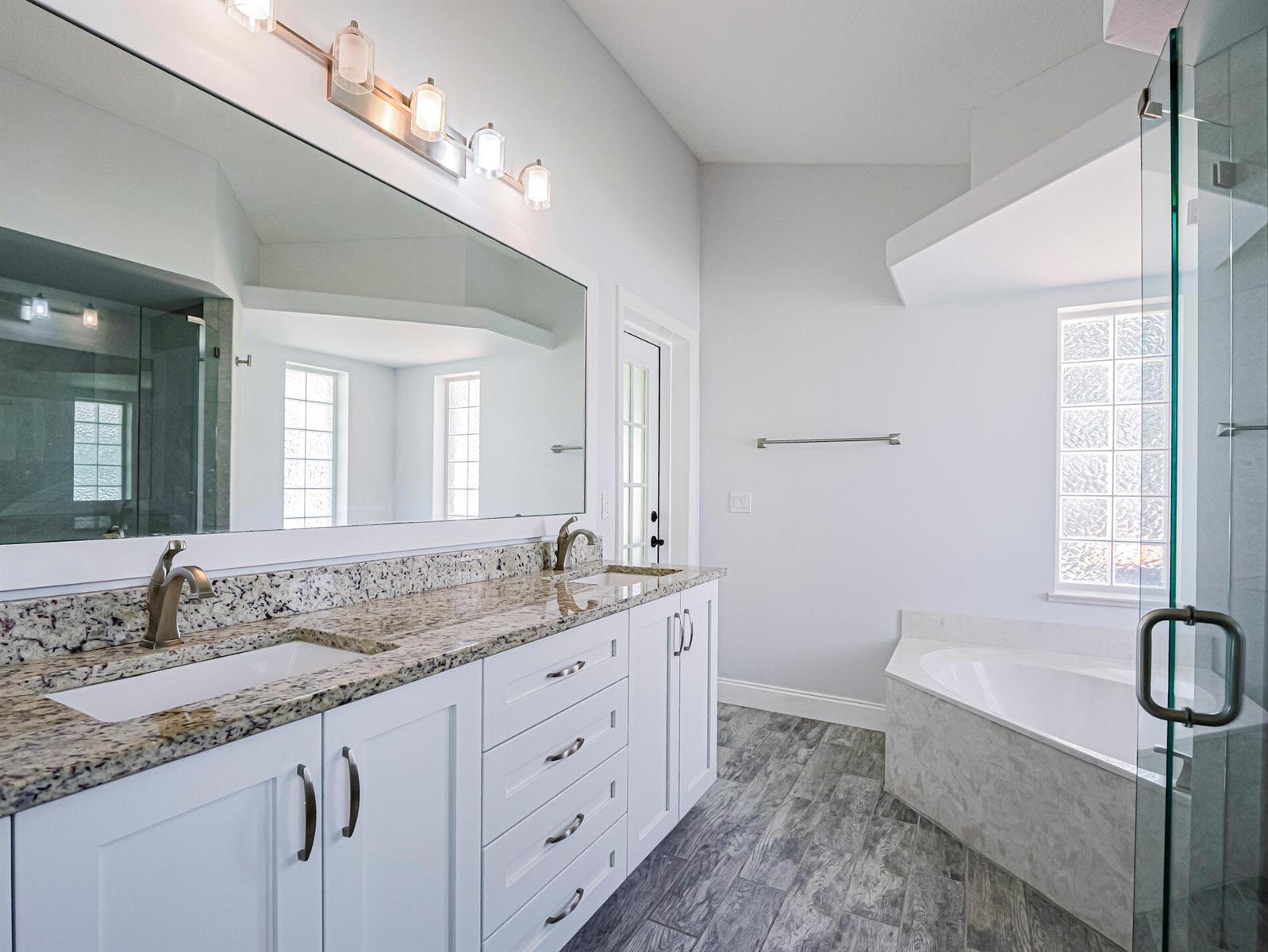 A bathroom features a double vanity with granite countertops, white cabinets, and a soaking tub — 725 23rd Avenue, Vero Beach FL 32962, VERO BEACH, FL