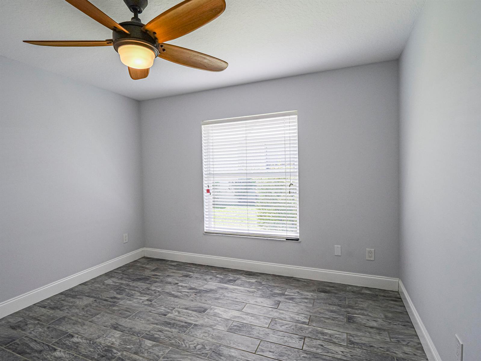 An empty room features light gray walls, wood-look tile flooring, and a ceiling fan — 725 23rd Avenue, Vero Beach FL 32962, VERO BEACH, FL