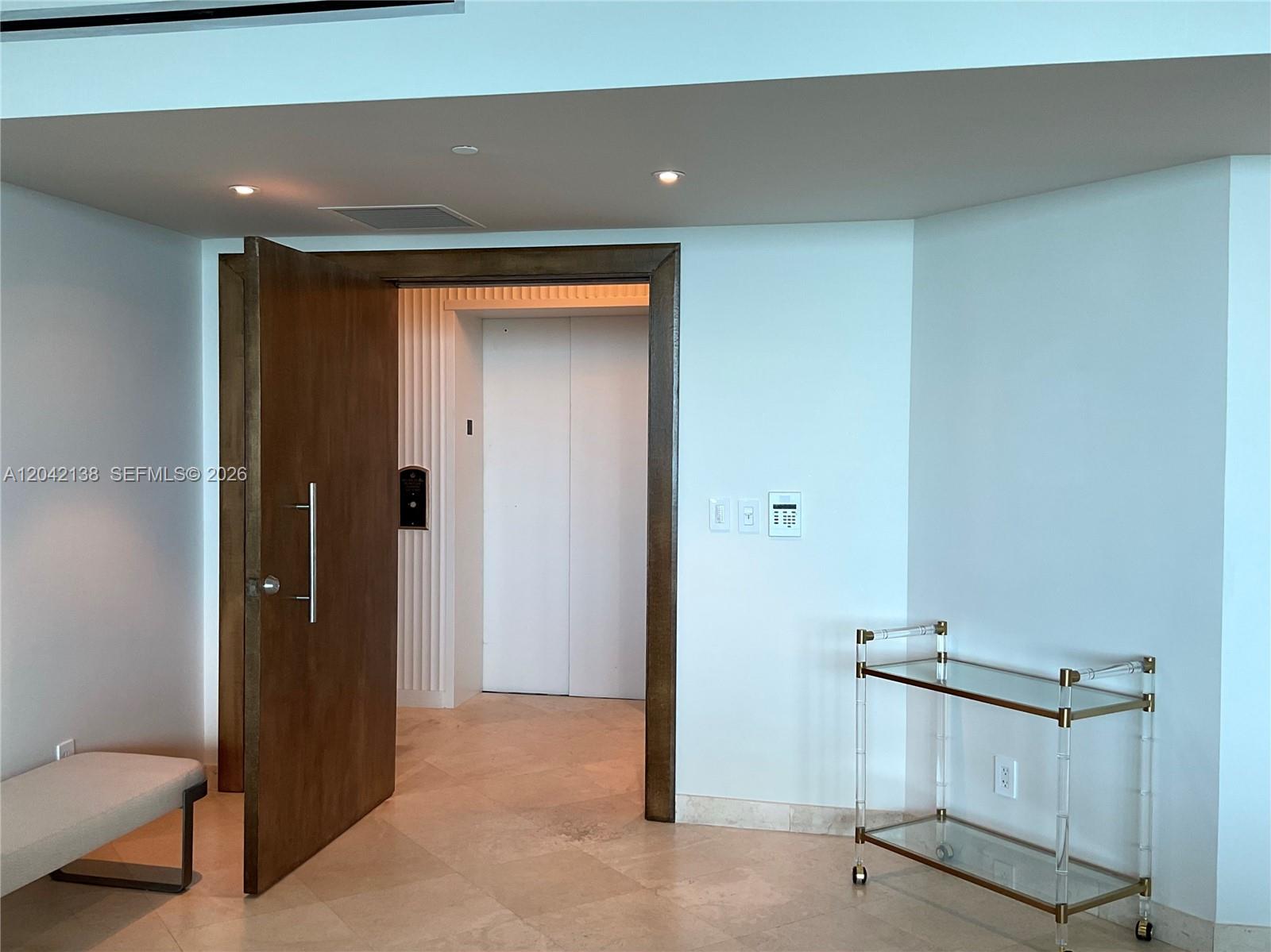 A wooden door opens to a private elevator foyer with a glass bar cart nearby — 1643 Brickell Ave # 2603, Miami FL 33129, MIAMI, FL