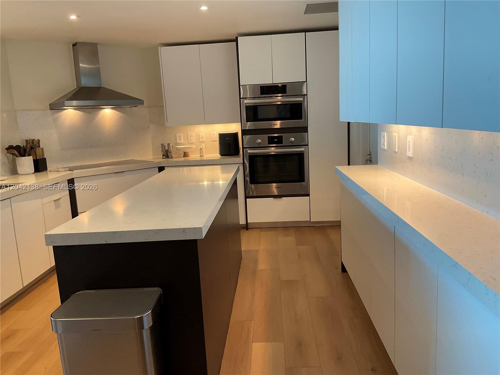 A modern kitchen features white cabinetry, a dark island, stainless steel appliances, and light flooring — 1643 Brickell Ave # 2603, Miami FL 33129, MIAMI, FL