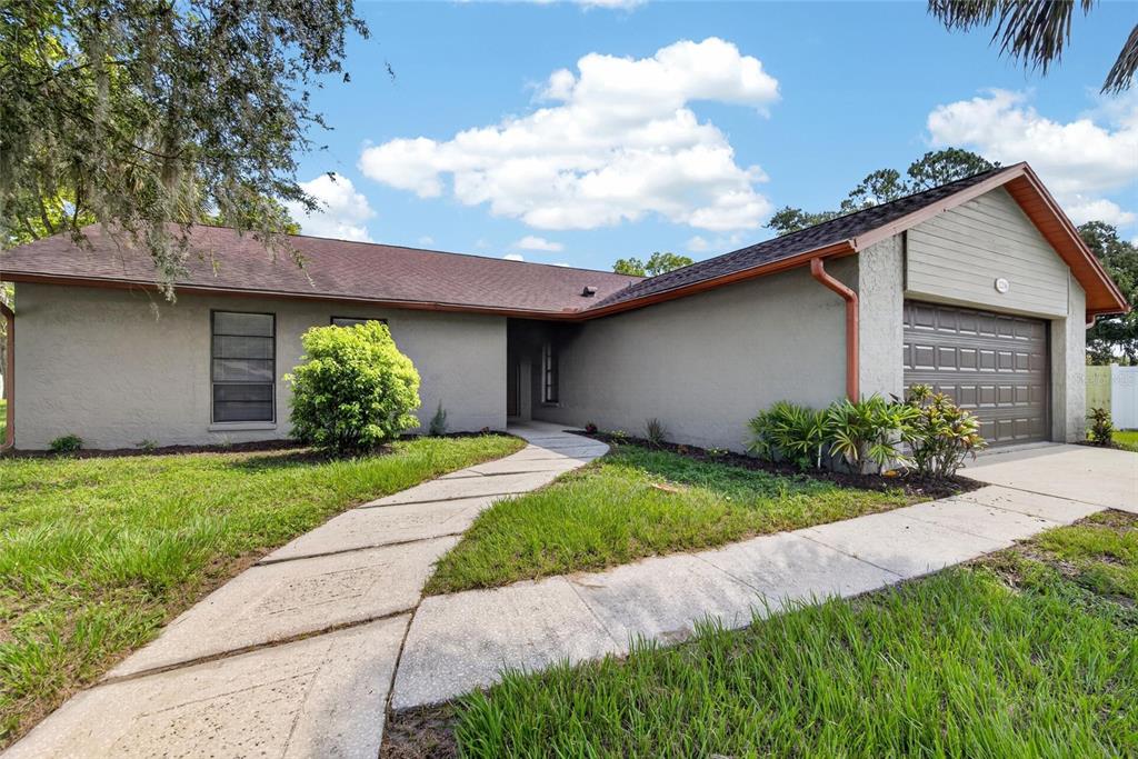 A single-story house with a gray stucco exterior, brown roof, and a curved concrete walkway — 1206 SAIL WAY, VALRICO, FL