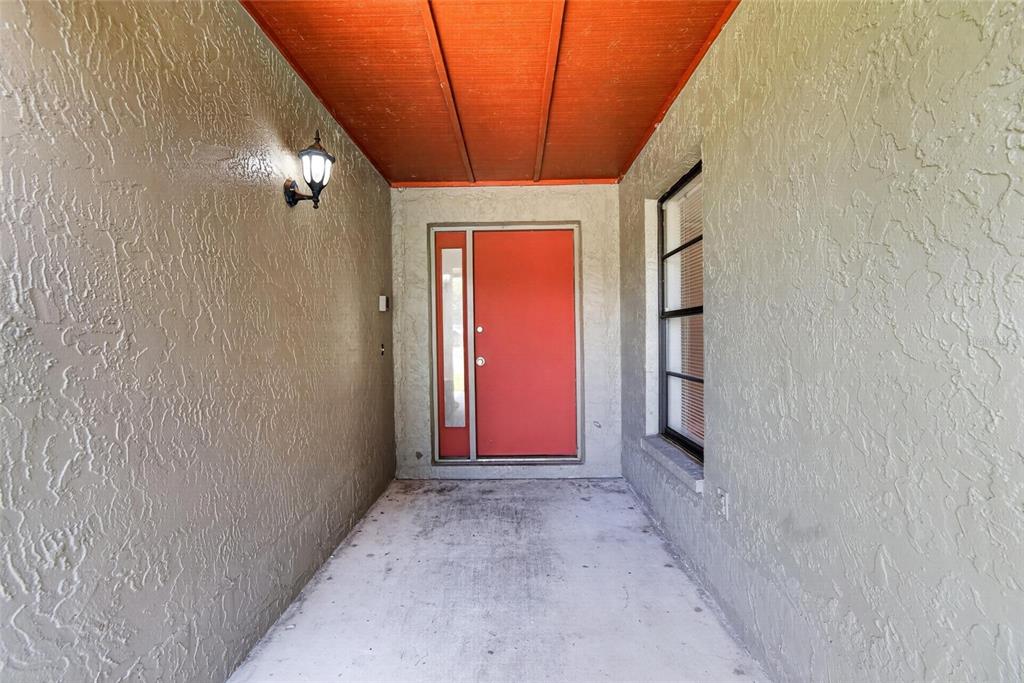 A covered entryway features a red front door, a side window, and textured beige walls — 1206 SAIL WAY, VALRICO, FL