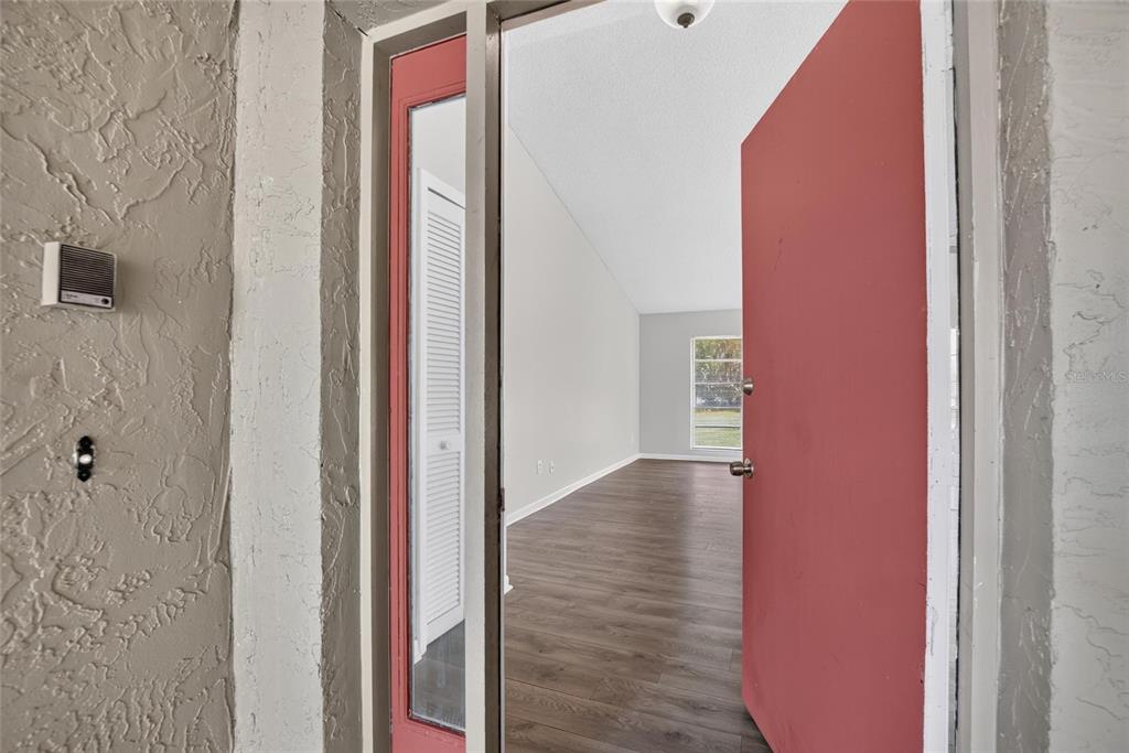 An open red front door reveals a living room with wood-look flooring and vaulted ceilings — 1206 SAIL WAY, VALRICO, FL