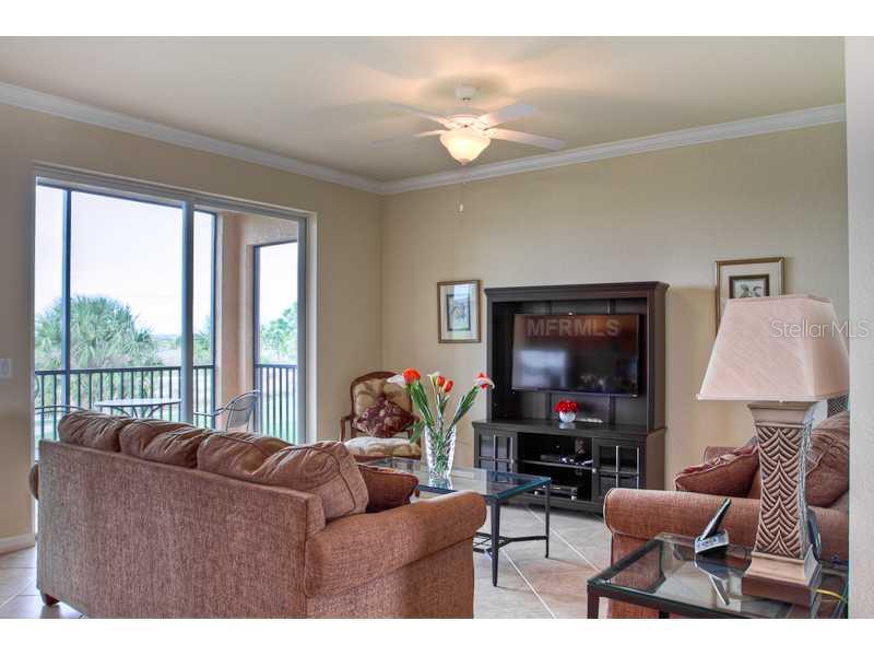 A living room features a brown sofa, a television console, and a sliding glass door — 8309 GRAND ESTUARY TRAIL UNIT 206, BRADENTON, FL