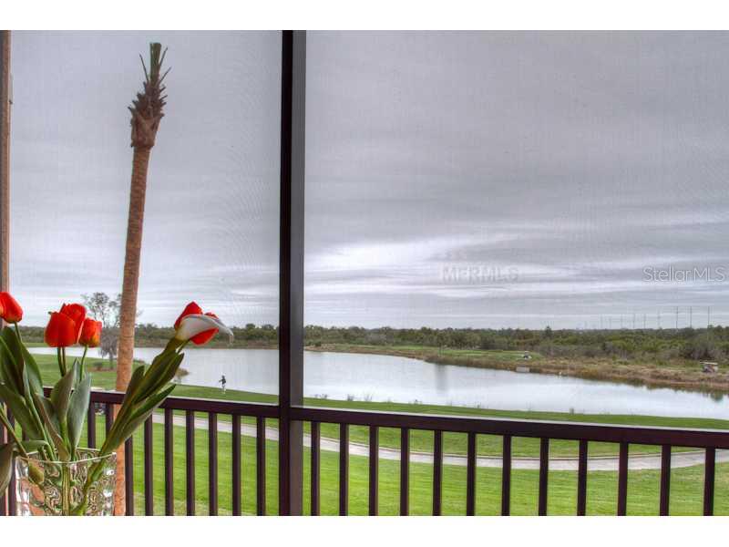 A view of a lake and golf course from a screened-in porch with flowers — 8309 GRAND ESTUARY TRAIL UNIT 206, BRADENTON, FL