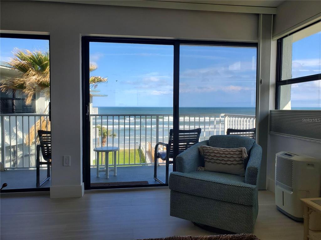 A living area with a patterned armchair faces a sliding glass door overlooking the ocean — 1571 S ATLANTIC AVENUE UNIT 405, NEW SMYRNA BEACH, FL