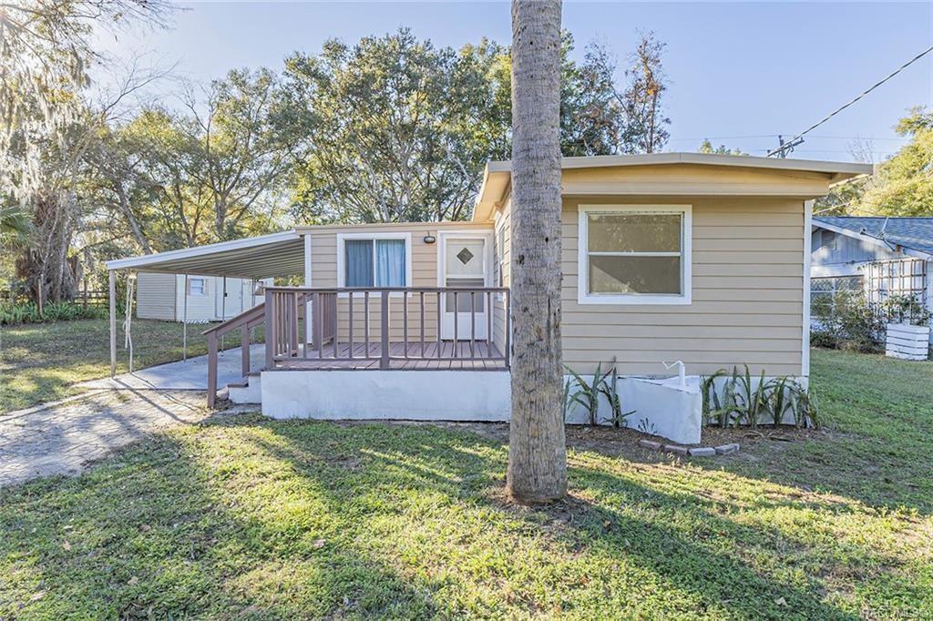 A tan mobile home features a front deck, a metal carport, and a palm tree — 1672 S CANARY TERRACE, INVERNESS, FL
