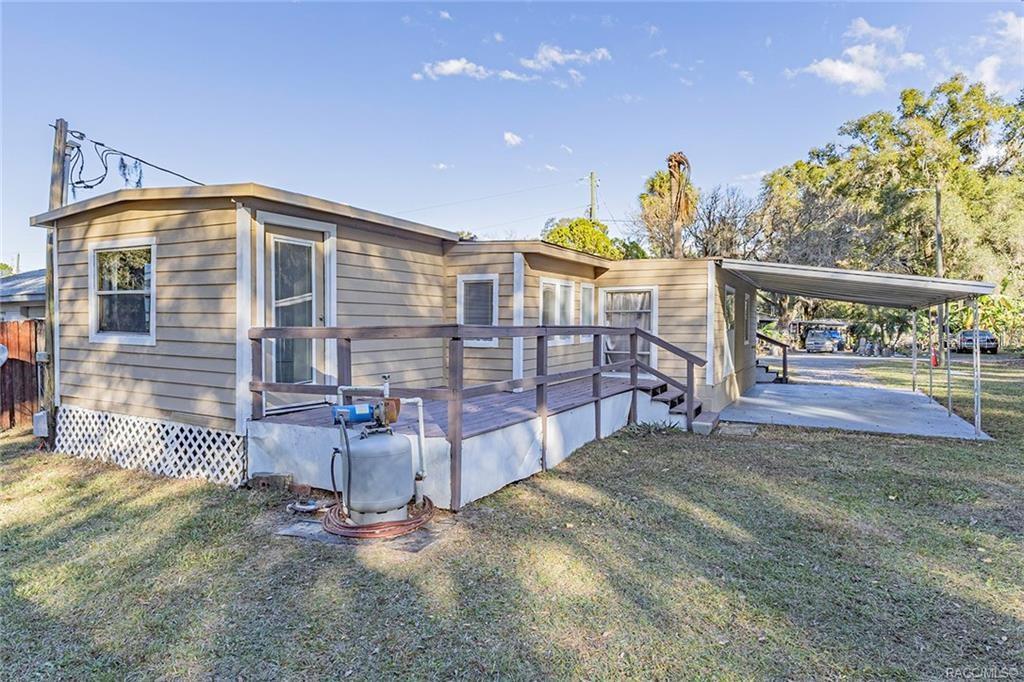 An exterior view of a tan mobile home with a wooden deck and metal carport — 1672 S CANARY TERRACE, INVERNESS, FL