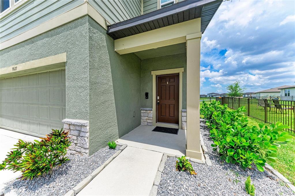 The exterior of a house features a brown front door, a garage, and landscaping — 9027 WAXWING WAY, PARRISH, FL