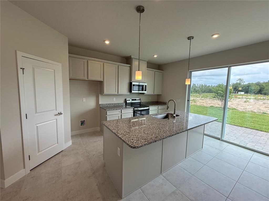 A kitchen features light-colored cabinets, granite countertops, a center island, and a sliding glass door — 1247 PINEYWOOD FIELD DRIVE, DAVENPORT, FL