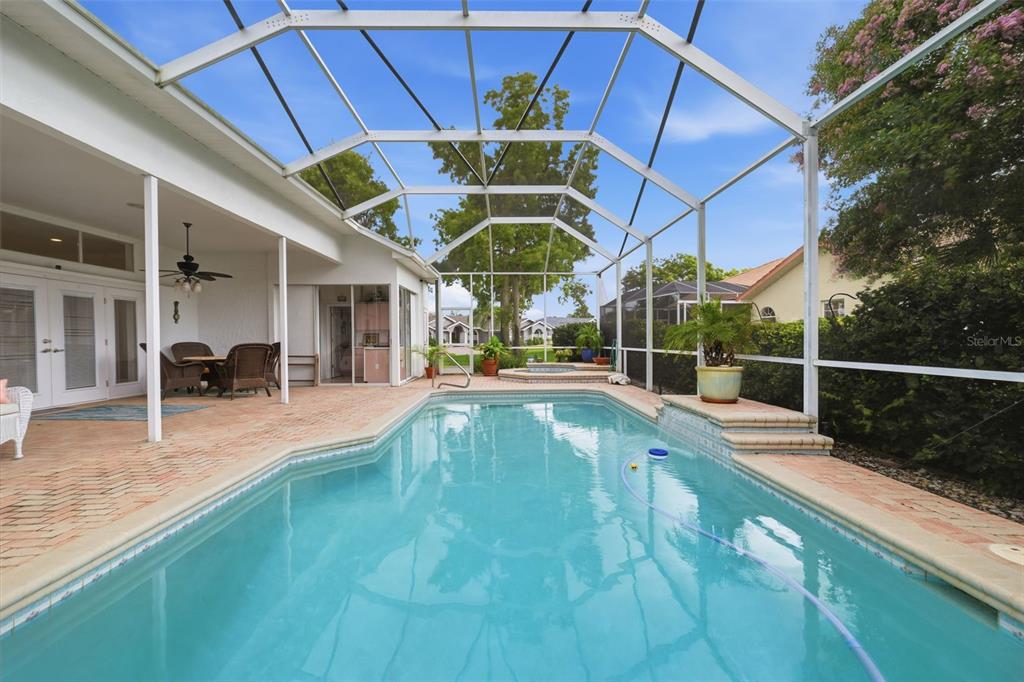 A screened-in patio features a rectangular swimming pool, a hot tub, and brick pavers — 13745 WOODWARD DRIVE, HUDSON, FL