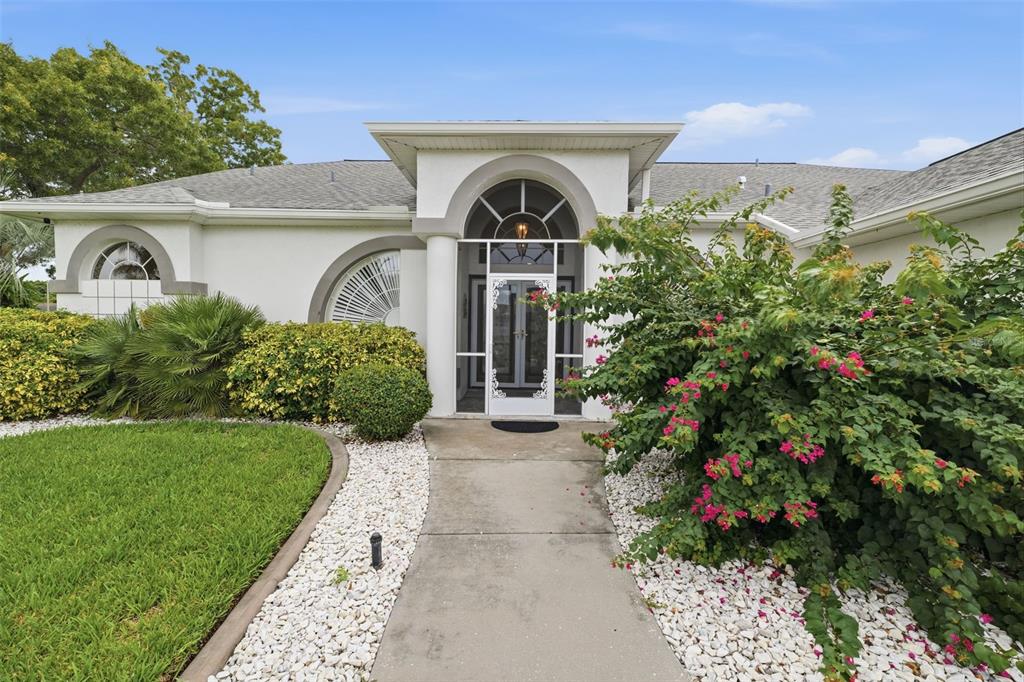 A white house exterior features a concrete walkway, arched entryway, and a large flowering bush — 13745 WOODWARD DRIVE, HUDSON, FL