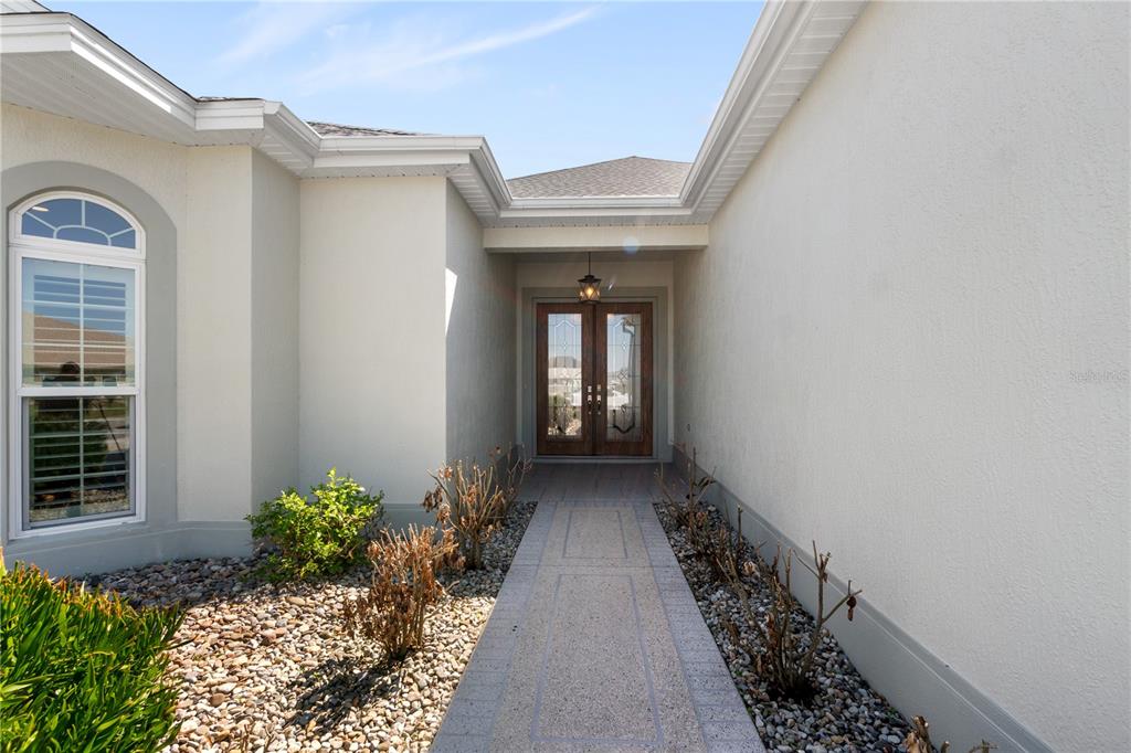 A paved walkway leads to the double front doors of a house with stucco walls — 5845 STORMS AVENUE, THE VILLAGES, FL