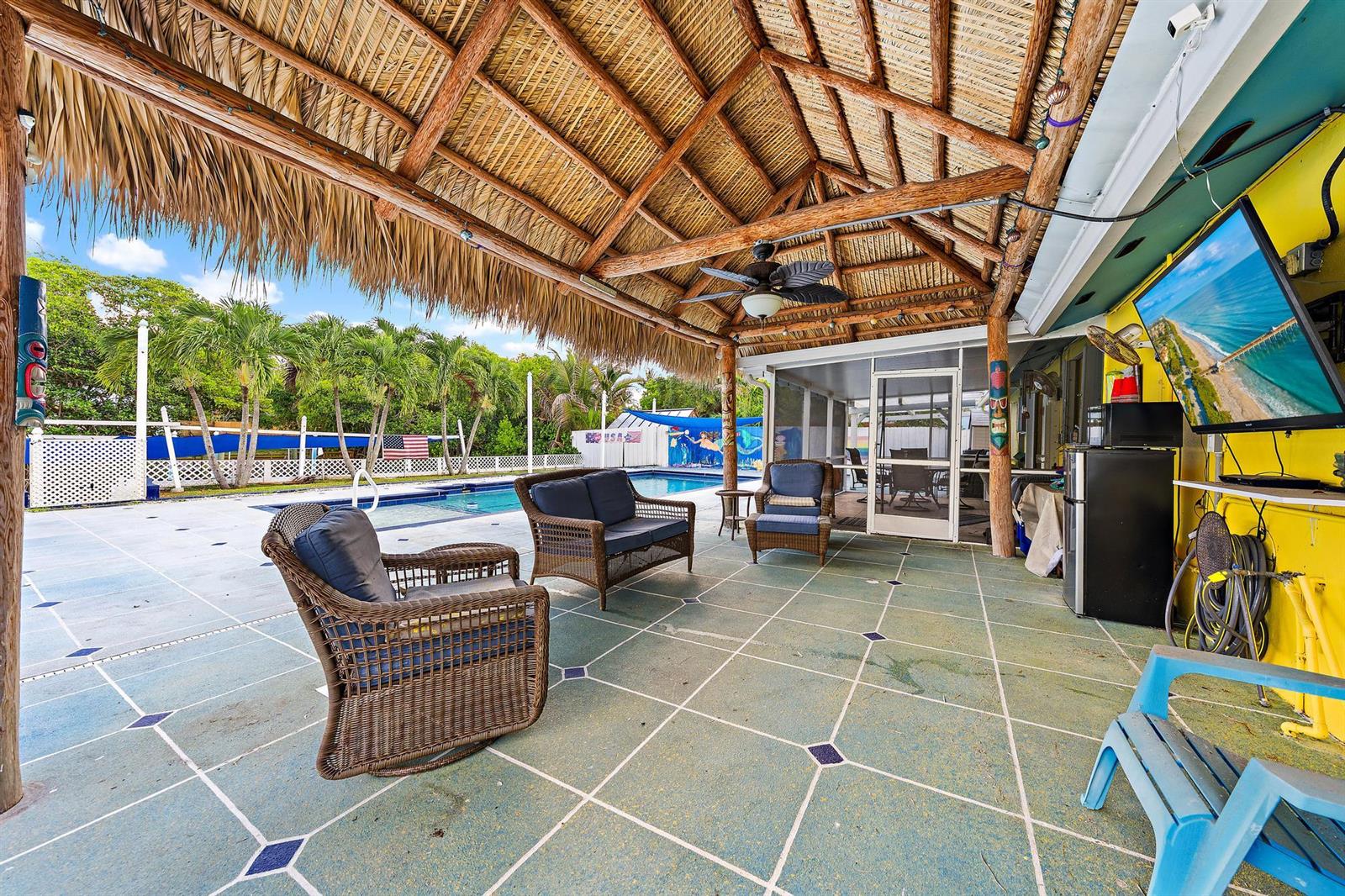 A covered patio with a thatched roof, wicker furniture, and a television overlooking a pool — 1005 Mohawk Street, Jupiter FL 33458, JUPITER, FL