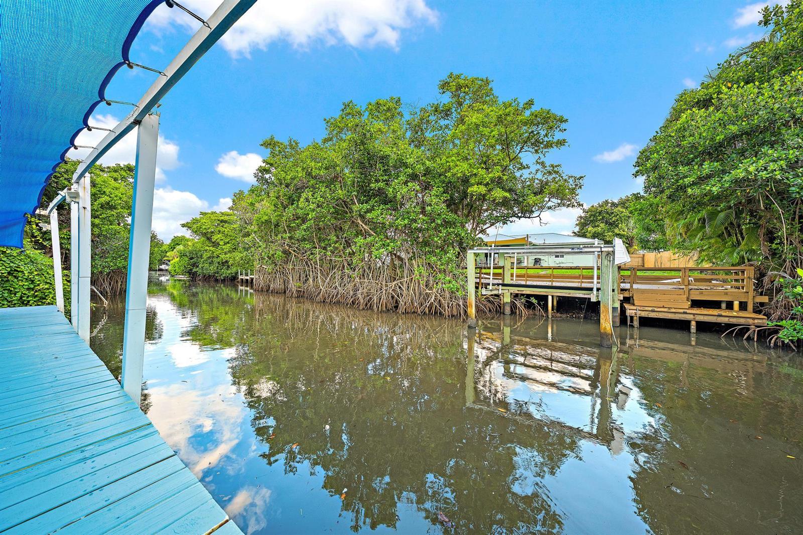 A blue wooden dock extends over a canal toward a wooden deck and mangroves — 1005 Mohawk Street, Jupiter FL 33458, JUPITER, FL