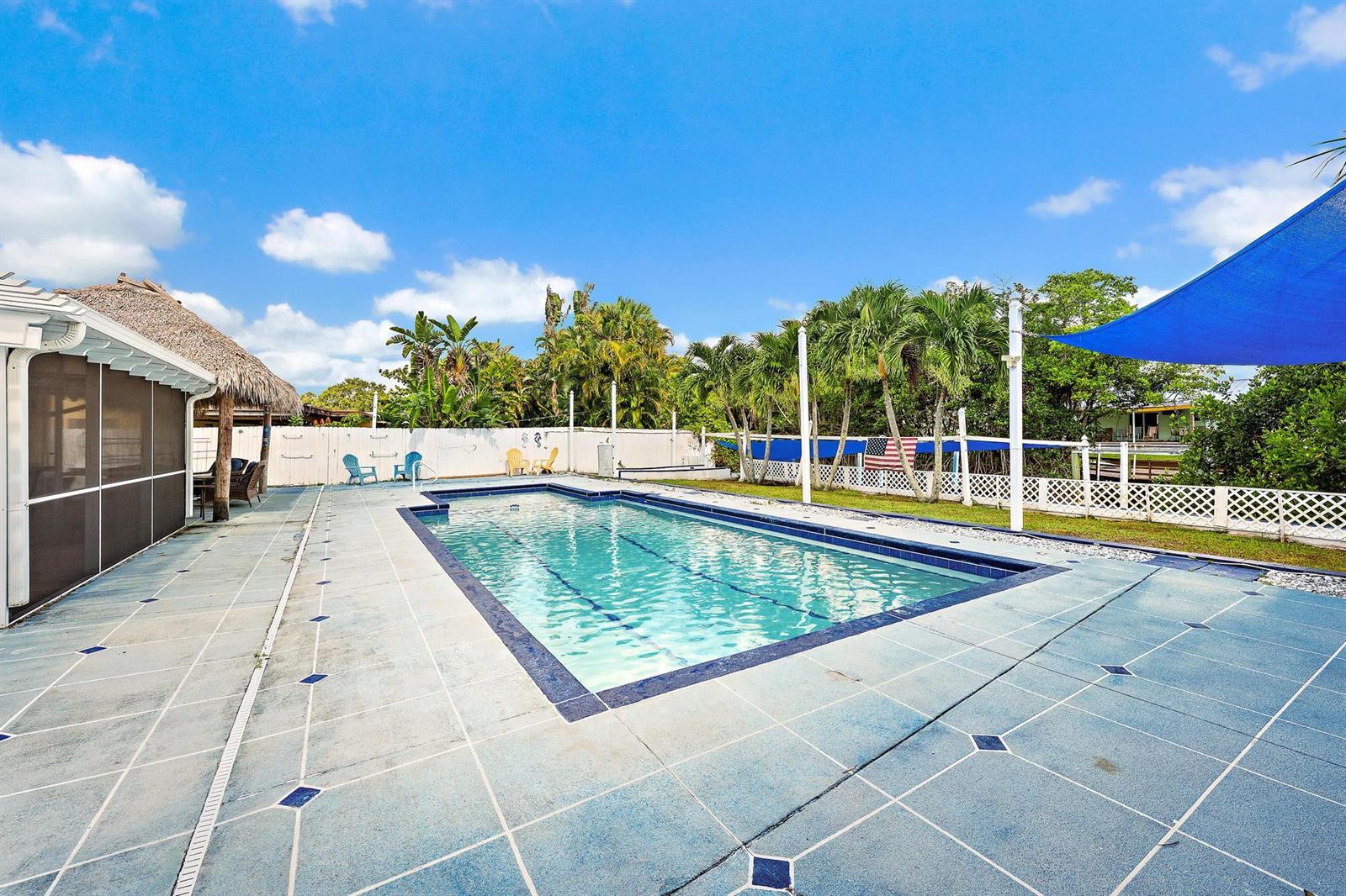 An outdoor swimming pool with a tiled deck, tiki hut, and blue shade sail — 1005 Mohawk Street, Jupiter FL 33458, JUPITER, FL