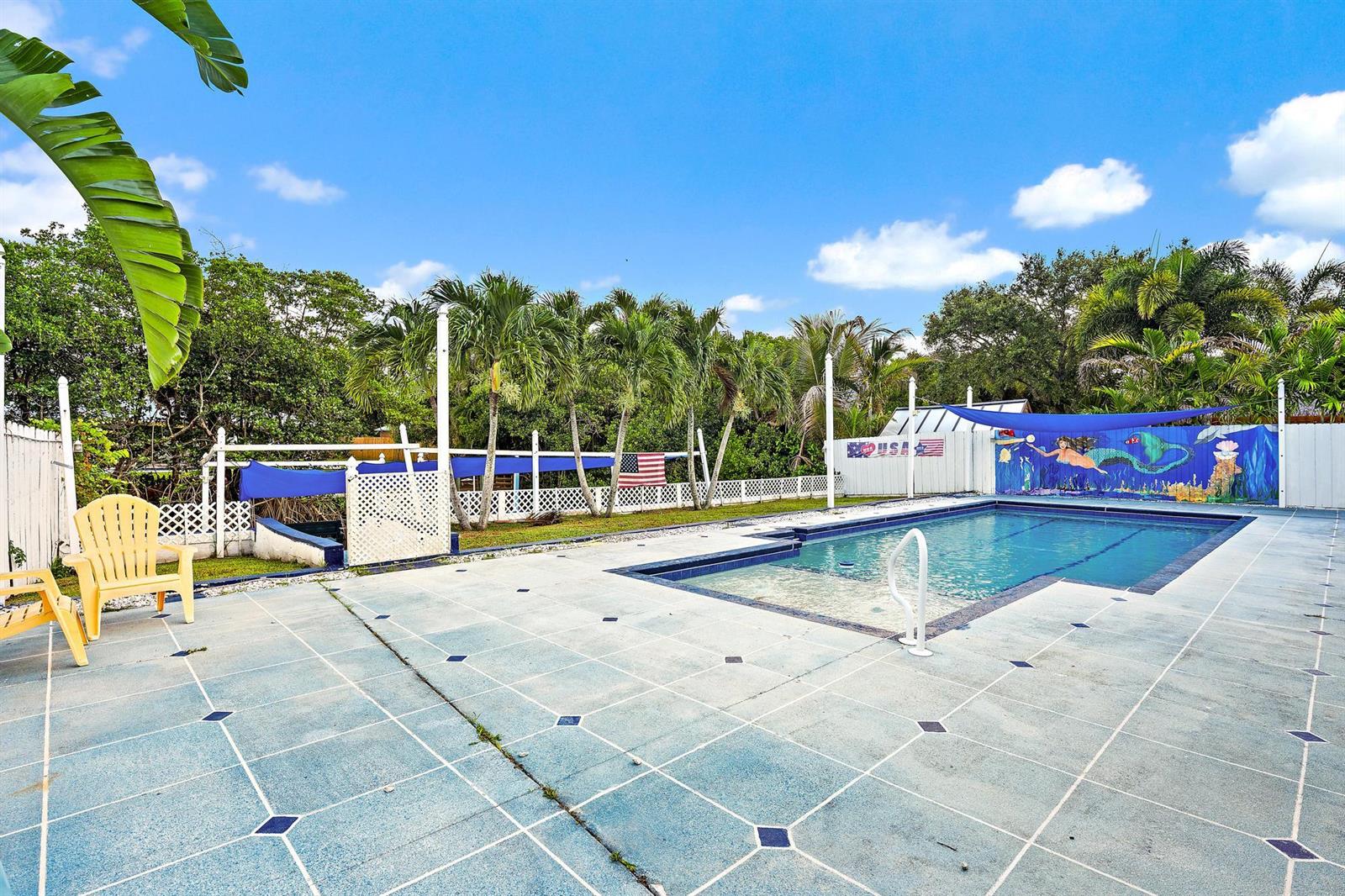 An outdoor swimming pool with a blue tiled deck, a mural, and palm trees — 1005 Mohawk Street, Jupiter FL 33458, JUPITER, FL