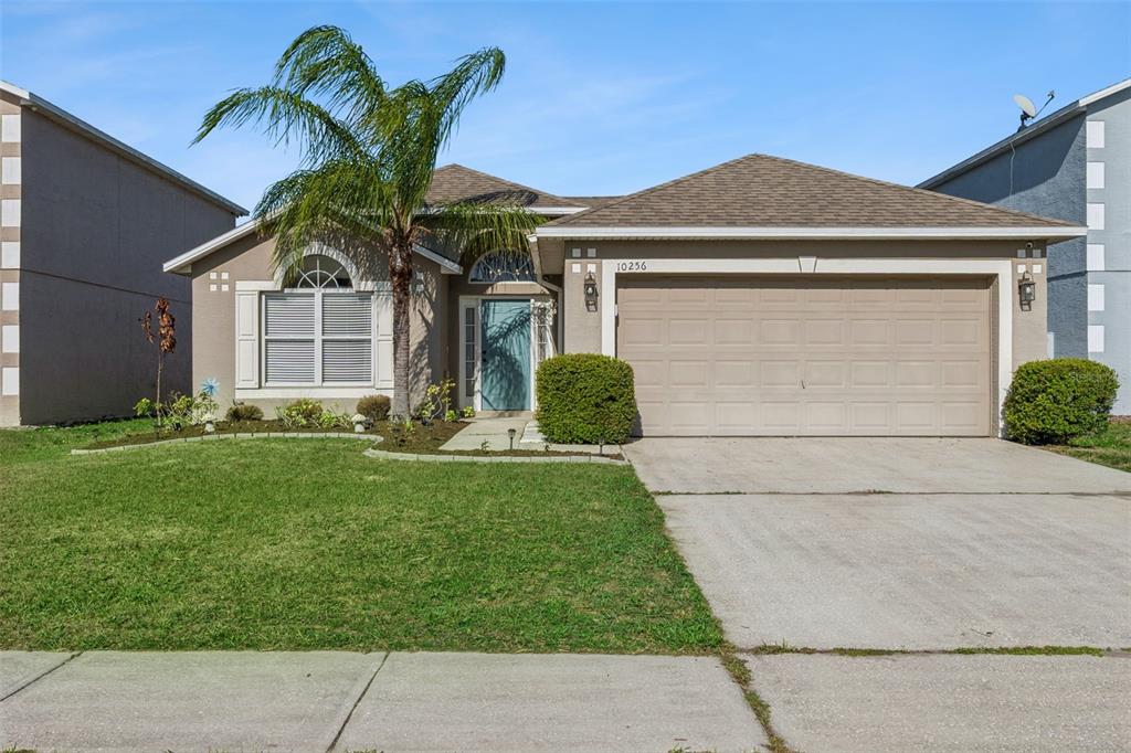 A single-story suburban house with a tan stucco exterior, a palm tree, and a garage — 10256 LAXTON STREET, ORLANDO, FL