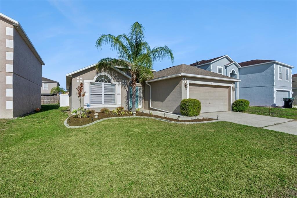 A single-story suburban house with a tan stucco exterior, a palm tree, and a garage — 10256 LAXTON STREET, ORLANDO, FL