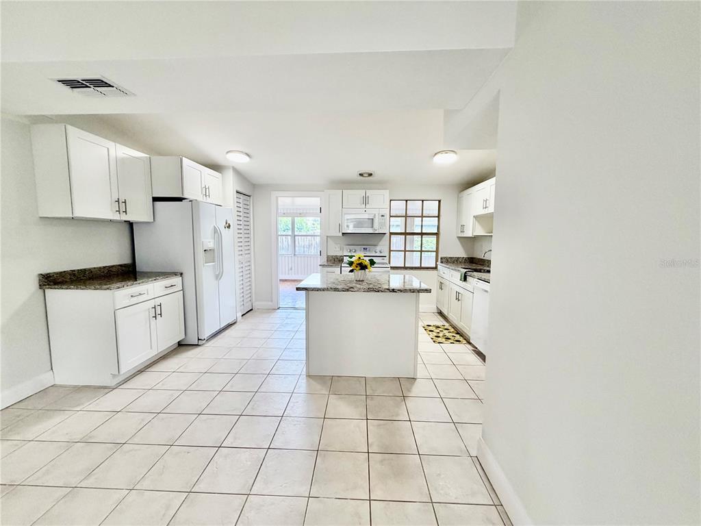 A kitchen features white cabinets, granite countertops, a central island, and light-colored tile flooring — 505 GLAD ROAD, WINTER HAVEN, FL