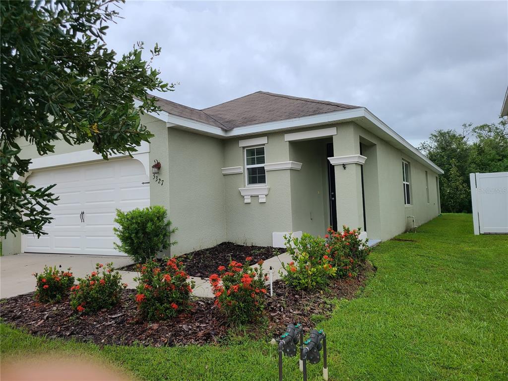 A single-story house with a light green stucco exterior, a two-car garage, and landscaped beds — 5327 SAN PALERMO DRIVE, BRADENTON, FL