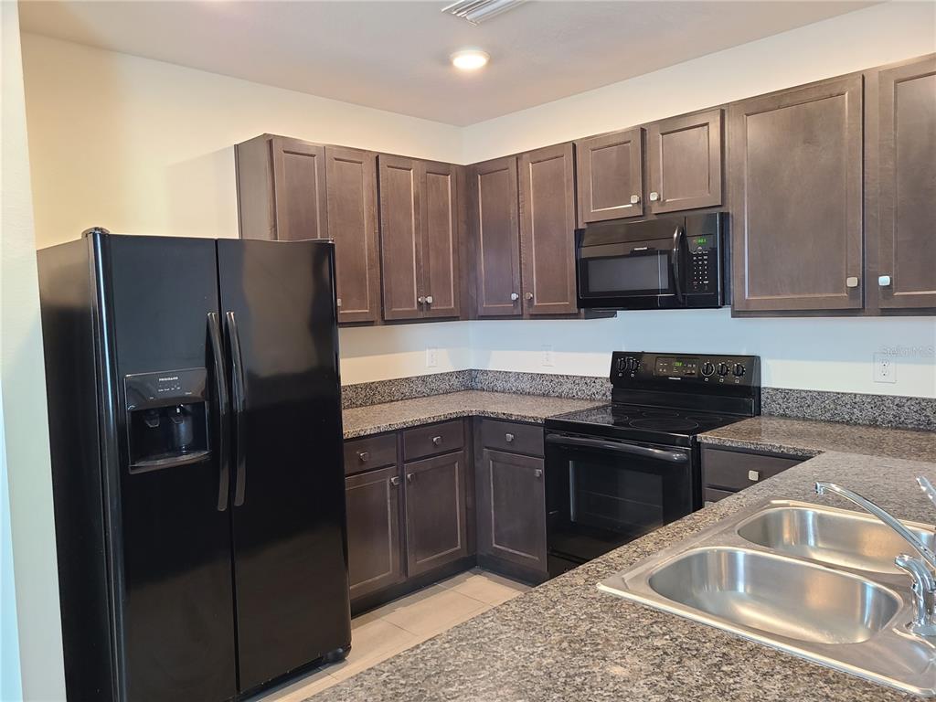A kitchen features dark wood cabinets, granite countertops, and black appliances — 5327 SAN PALERMO DRIVE, BRADENTON, FL