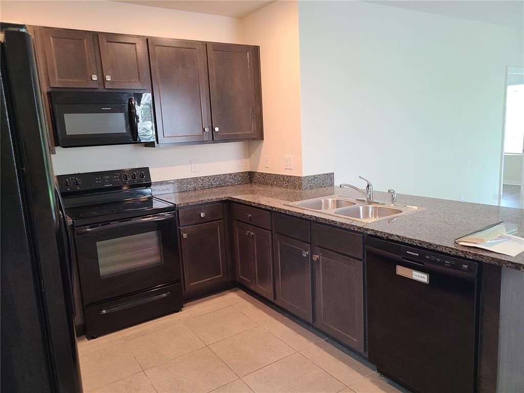 A kitchen features dark wood cabinets, granite countertops, black appliances, and light tile flooring — 5327 SAN PALERMO DRIVE, BRADENTON, FL