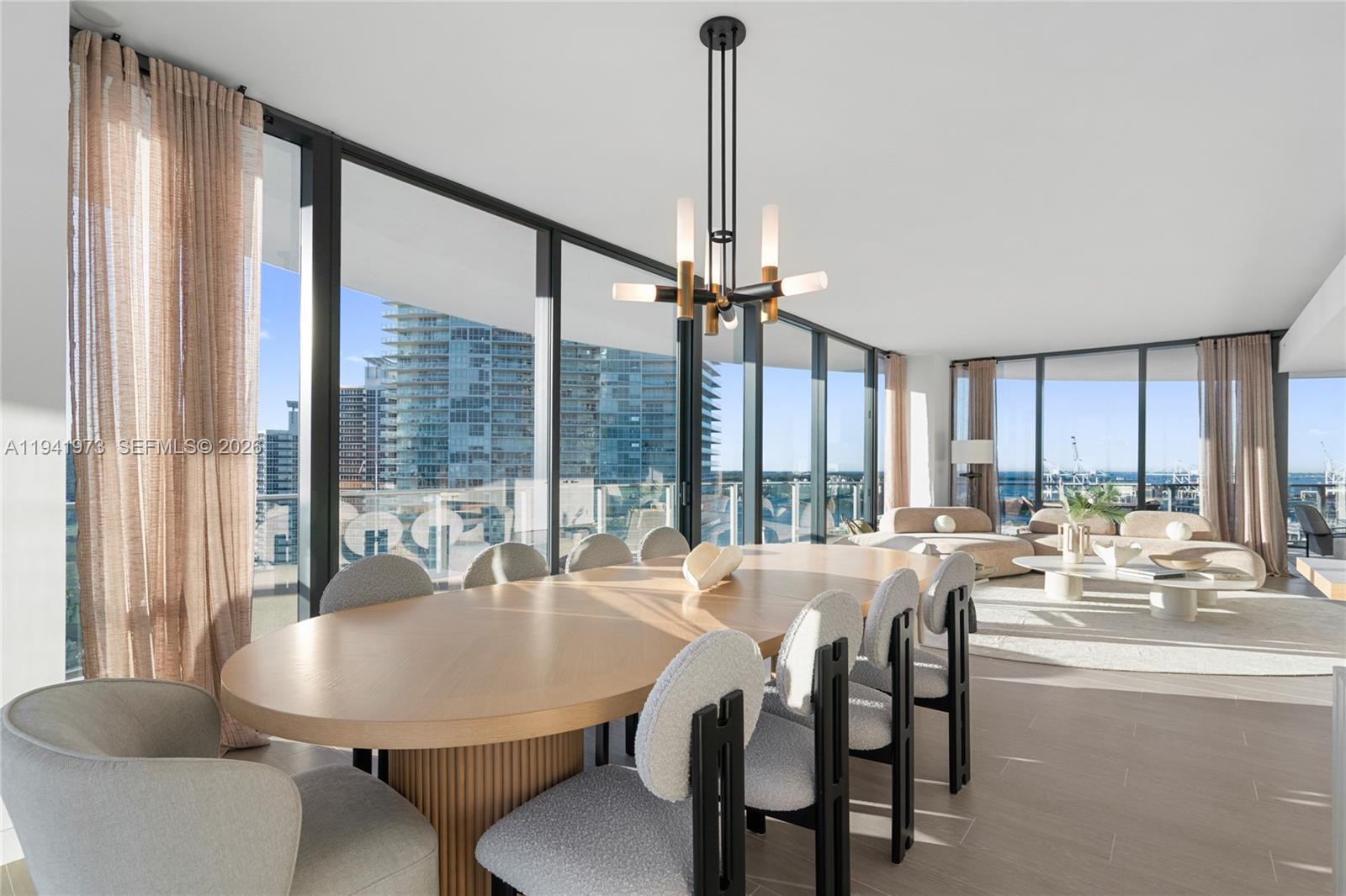 A dining area with a wooden table and chairs sits before floor-to-ceiling windows overlooking buildings — 500 Alton Rd, Miami Beach FL 33139, MIAMI BEACH, FL