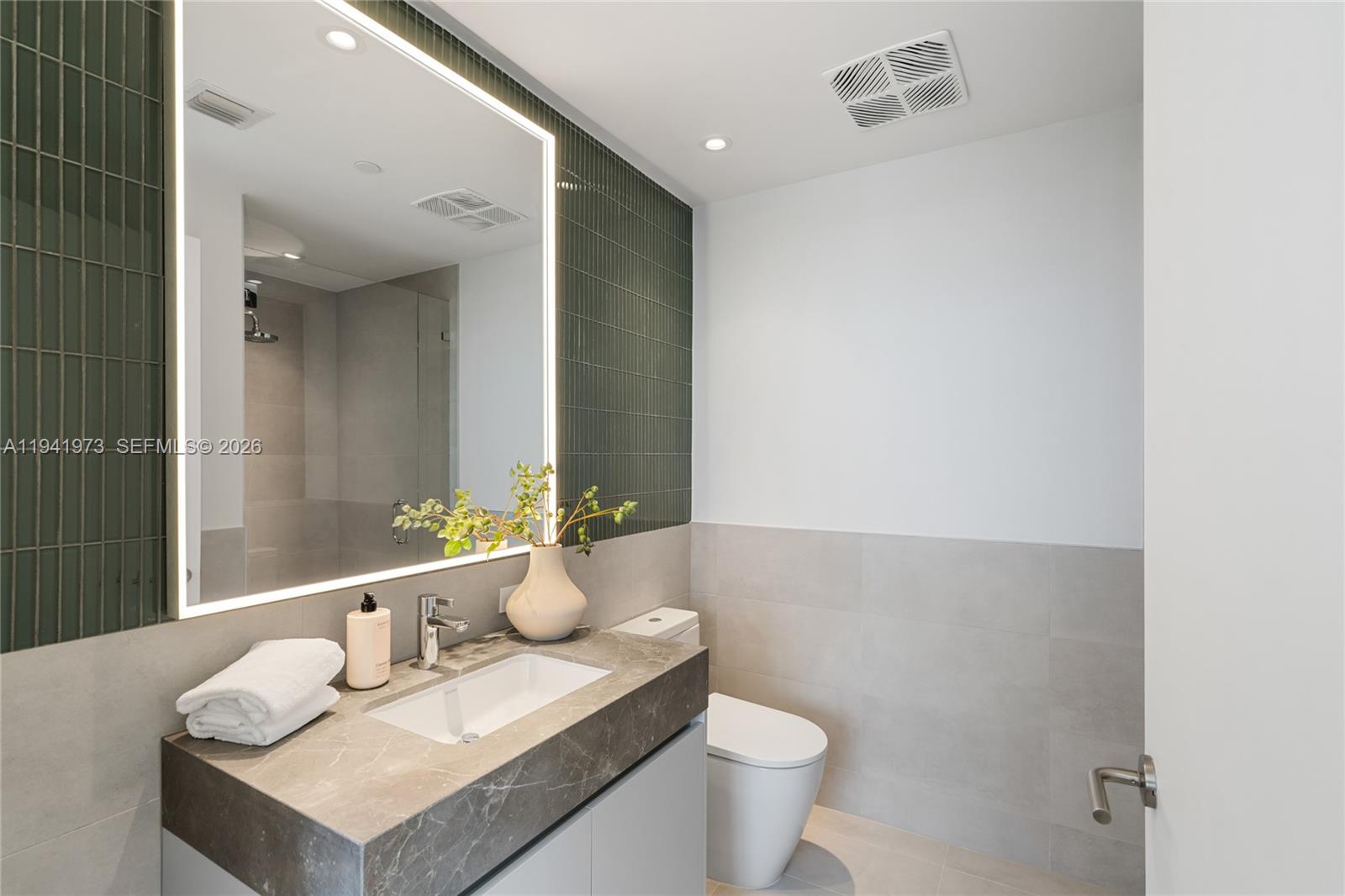 A modern bathroom features a stone vanity, a backlit mirror, and green vertical wall tiles — 500 Alton Rd, Miami Beach FL 33139, MIAMI BEACH, FL