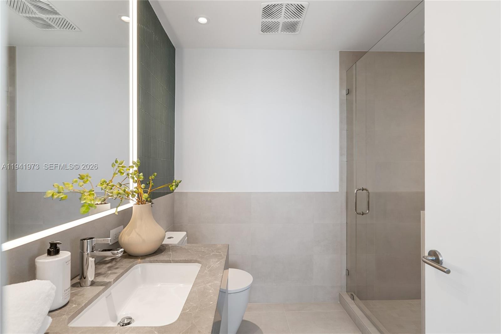 A modern bathroom features a stone vanity, a glass-enclosed shower, and a large backlit mirror — 500 Alton Rd, Miami Beach FL 33139, MIAMI BEACH, FL