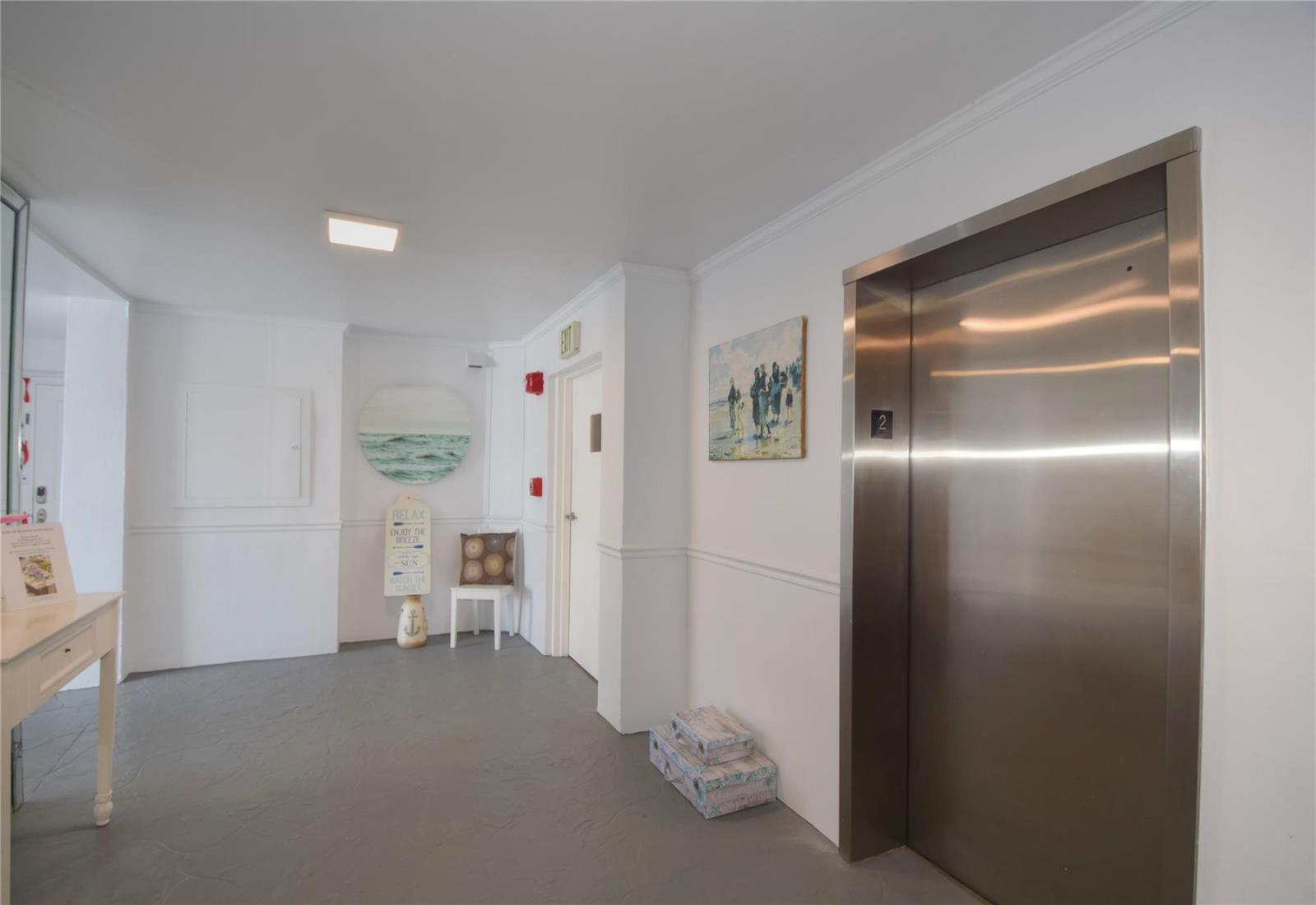 An elevator lobby with white walls, gray flooring, a small chair, and coastal-themed wall art — 1012 N Ocean Boulevard # 204, Pompano Beach FL 33062, POMPANO BEACH, FL
