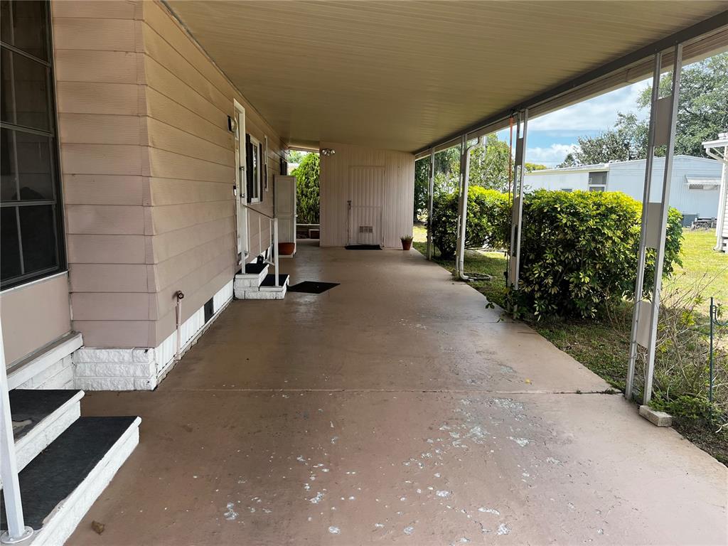 A covered concrete carport runs alongside the side of a tan mobile home — 192 PHILADELPHIA BOULEVARD UNIT 9, PALM HARBOR, FL