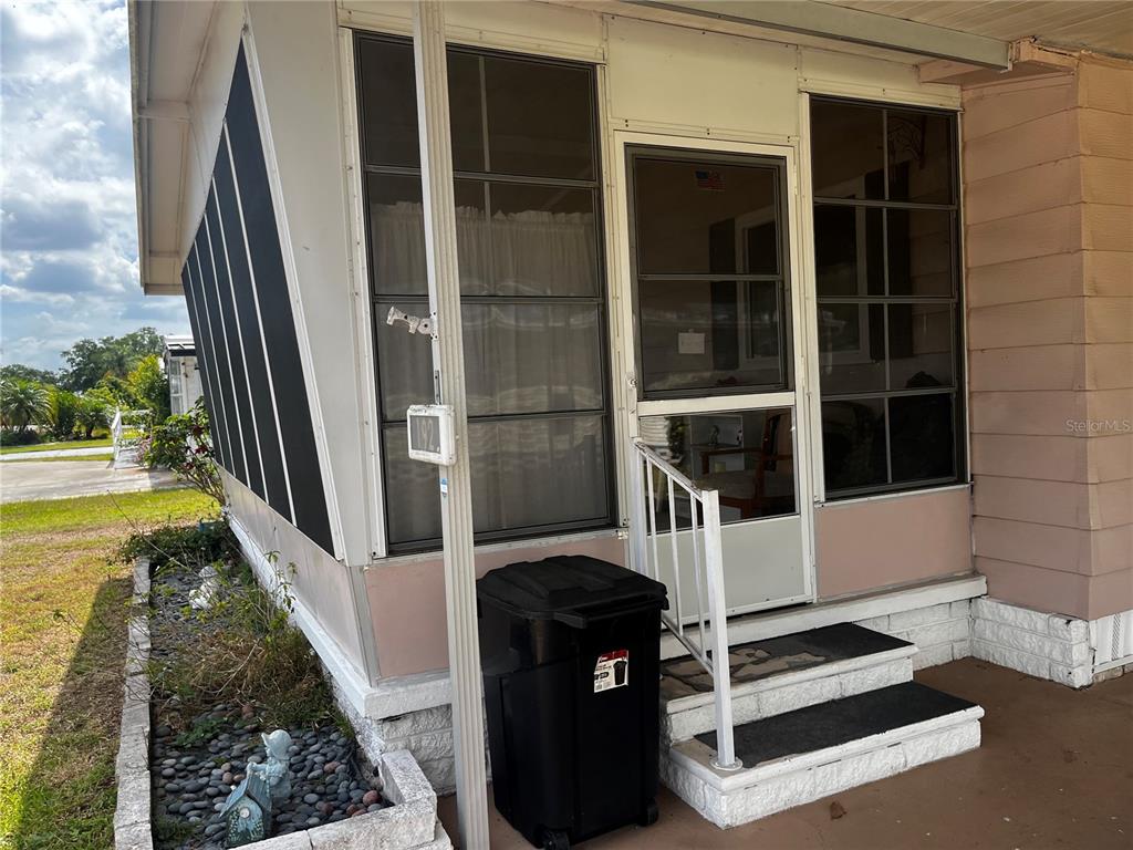 The exterior of a mobile home features a screened-in porch with steps and a trash bin — 192 PHILADELPHIA BOULEVARD UNIT 9, PALM HARBOR, FL